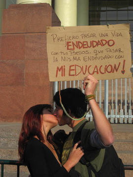 Pareja con cartel "PREFIERO PASAR UNA VIDA ENDEUDADO CON TUS BESOS, QUE PASAR LA MISMA ENDEUDADO CON MI EDUCACIÓN!"