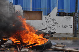 Barricada al frente de una pared con escrito "EL FUEGO RECLAMA POR VIVIR EN LIBERTAD"