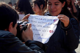 Mujer sosteniendo cartel de "Chile tiene el + alto gasto en insumos militares..."
