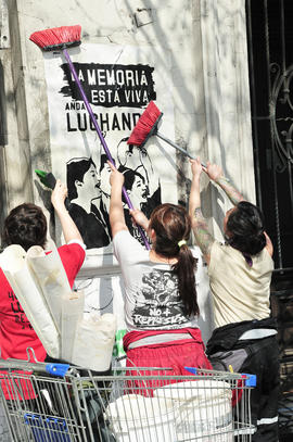 Mujeres pegando adiche "LA MEMORIA ESTÁ VIVA, ANDA LUCHANDO"